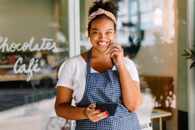 Empreendedora sorrindo enquanto usa o celular na gestão de sua pequena empresa