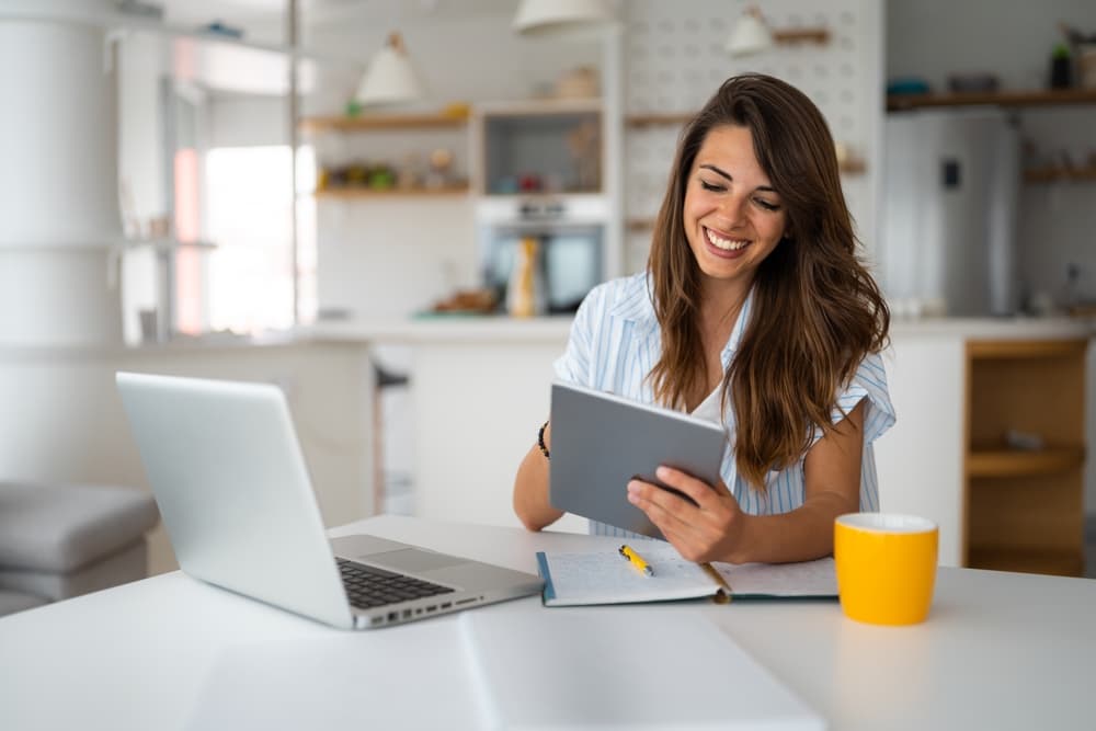 Mulher trabalhando com tablet e notebook enquanto empreende em casa