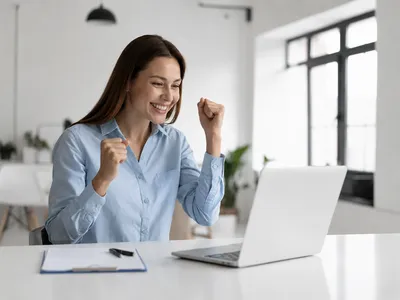 Empreendedora sorrindo na frente do computador ao organizar a gestão da sua pequena empresa
