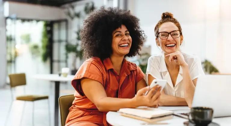 Mulheres trabalhando e sorrindo em ambiente profissional no Dia das Mulheres