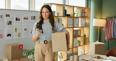 Microempresaria usando el celular para controlar pedidos y preparar envíos