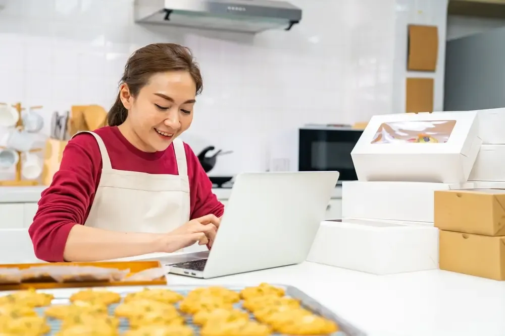 Empreendedora organizando pedidos de alimentos no computador durante a produção
