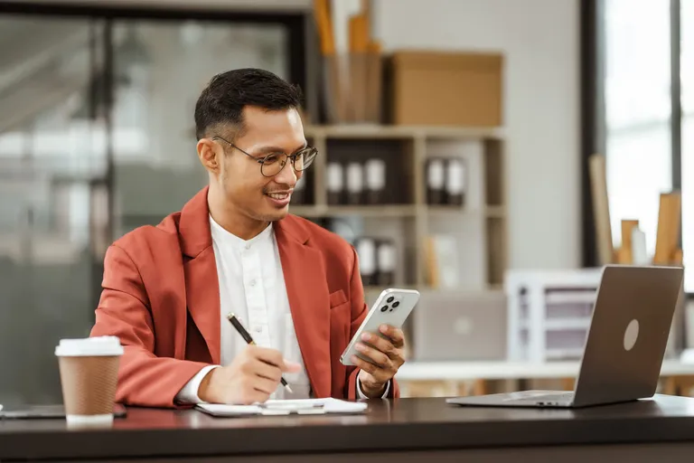 Emprendedor revisando el flujo de caja en el celular mientras toma notas