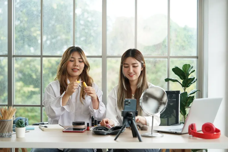 Duas mulheres gravando conteúdo para vender maquiagem online com produtos dispostos na mesa