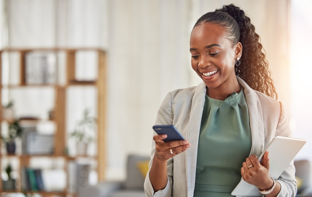 Empreendedora sorrindo ao usar smartphone para otimizar a gestão do seu negócio
