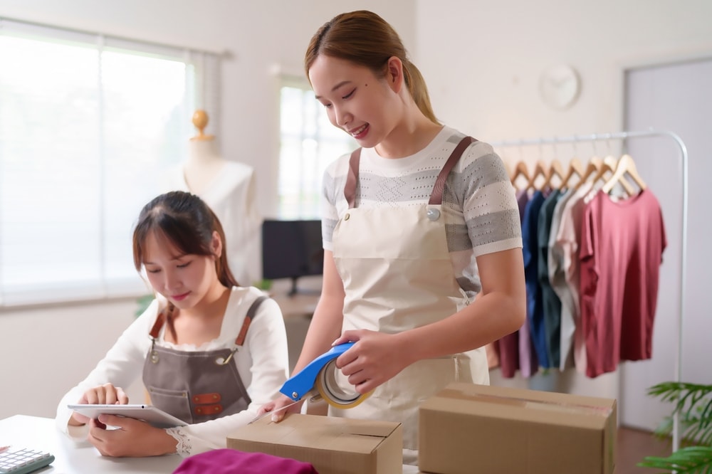 Empreendedoras organizando pedidos de clientes, conferindo produtos e embalando encomendas como parte da organização de pedidos no dia a dia do negócio.