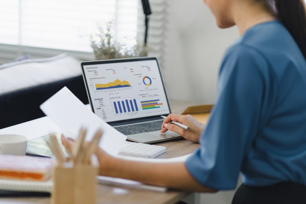 Mulher analisando relatórios de vendas no notebook com gráficos de desempenho e indicadores financeiros para tomada de decisão.