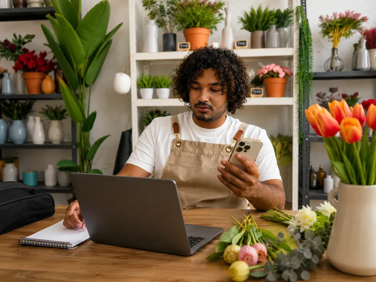 Empreendedor em floricultura verificando mensagem no celular para responder reclamação do cliente