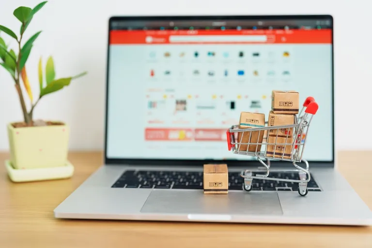 Carrinho de compras com caixas apoiado em um notebook aberto em página de e-commerce, representando a escolha entre marketplace ou vendas diretas.