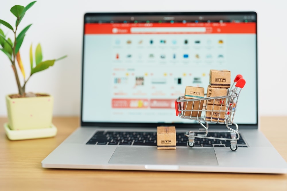 Carrinho de compras com caixas apoiado em um notebook aberto em página de e-commerce, representando a escolha entre marketplace ou vendas diretas.