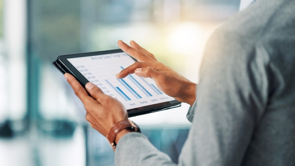 Pessoa analisando indicadores para pequenos negócios em um tablet, com gráficos e métricas de desempenho.