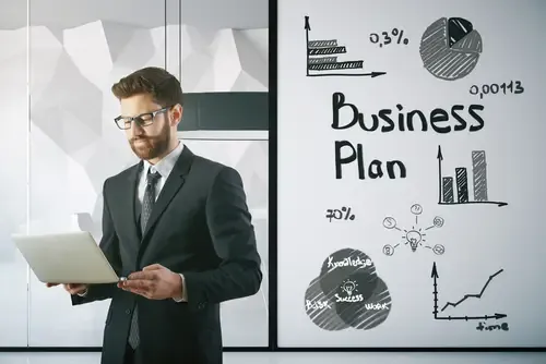 Empreendedor analisando plano de negócios no laptop ao lado de gráficos