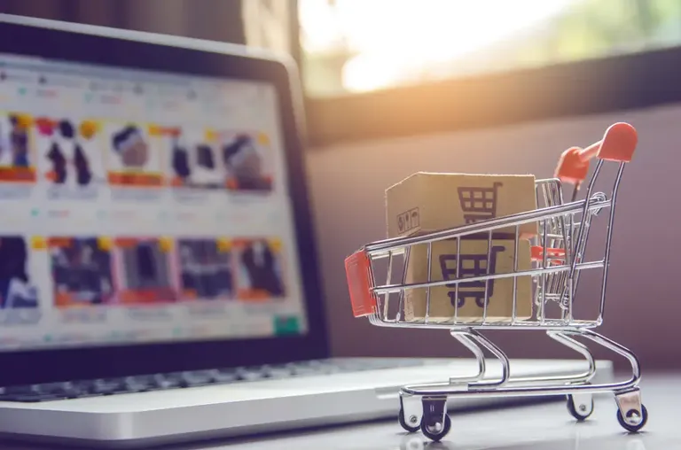 Carrinho com caixas diante de notebook representando criação de catálogo de produtos digital
